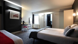 A hotel room with two beds, a desk, a chair, and a door leading to a bathroom. - Hotel La Royale (Leuven)