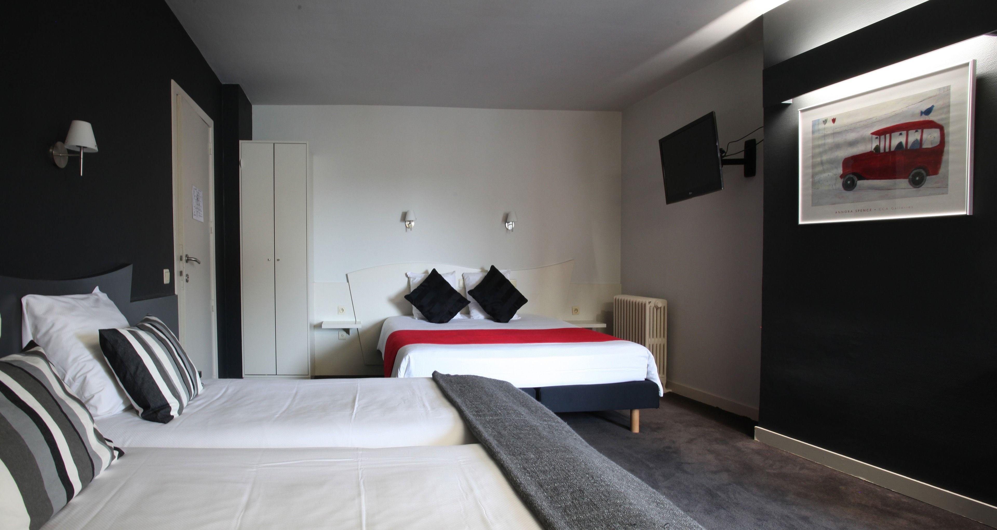 Hotellihuone, jossa on kaksi sänkyä, valkoinen vaatekaappi, patteri ja seinällä oleva kehystetty taulu.