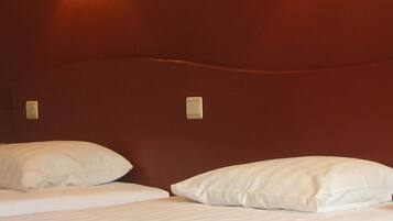 Habitación de hotel con dos camas, cada una con ropa de cama y almohadas blancas, y dos lámparas de pared que proporcionan luz.