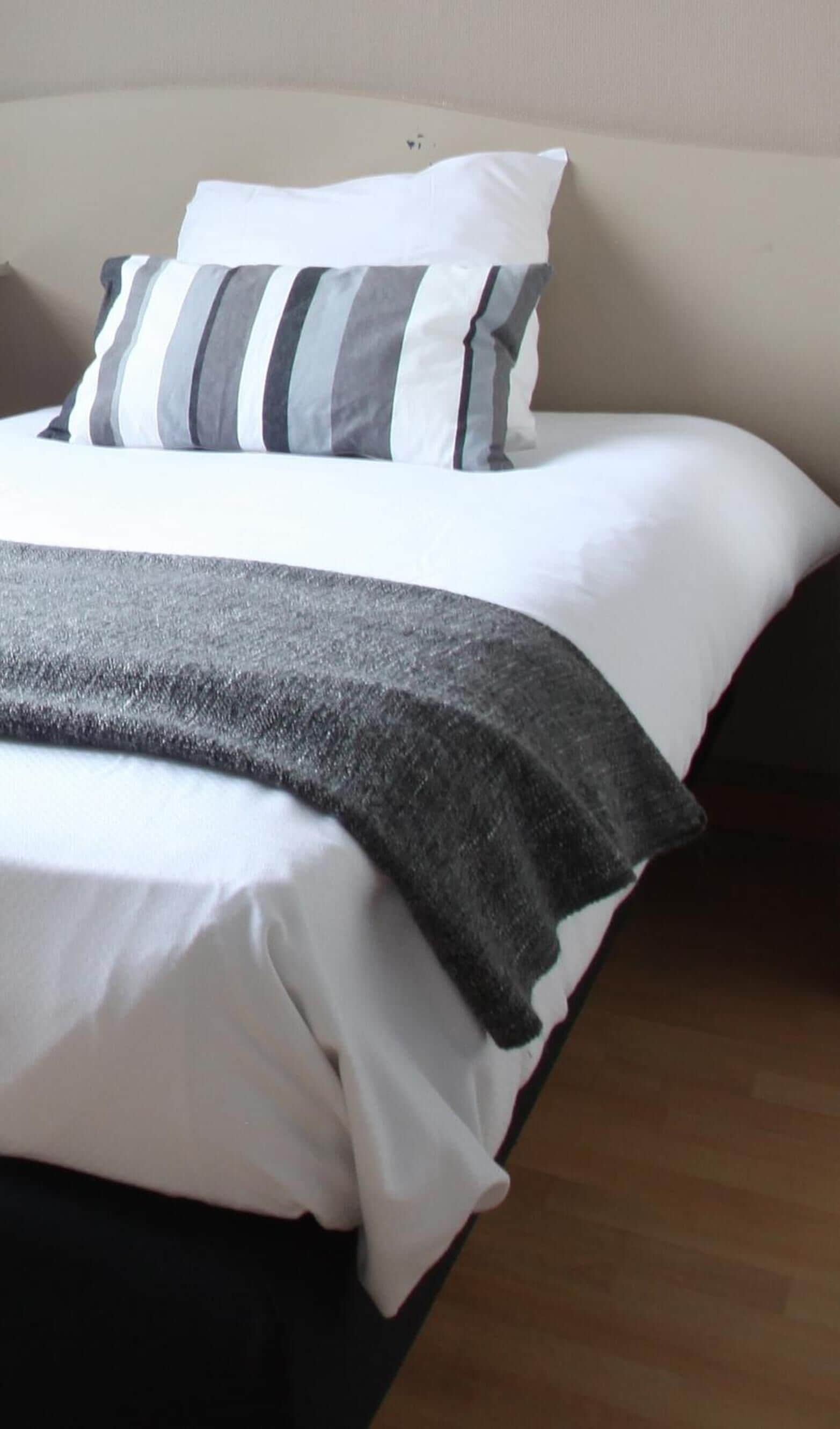 A bed with white and gray striped pillows and a gray blanket.