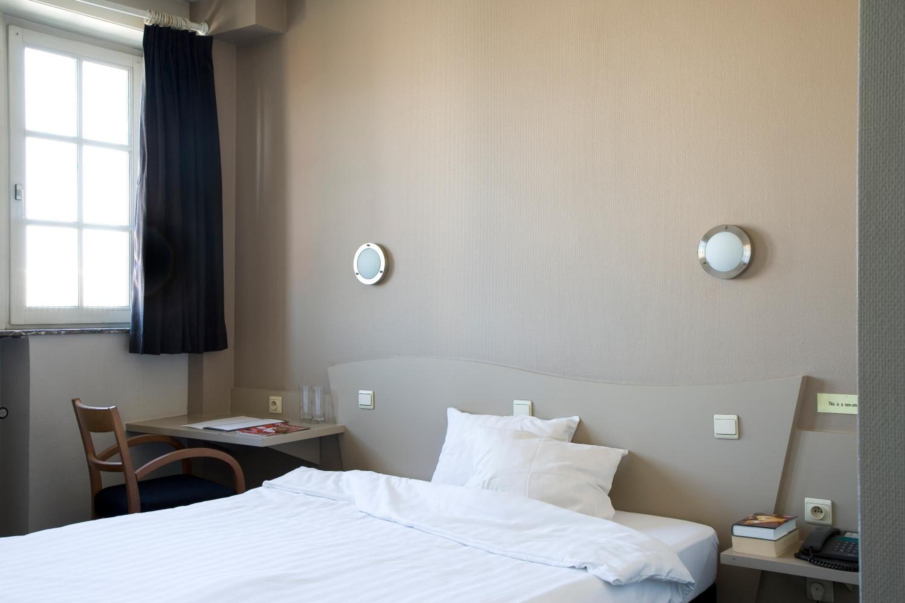 A hotel room with a bed, a desk, a chair, and a window with curtains.