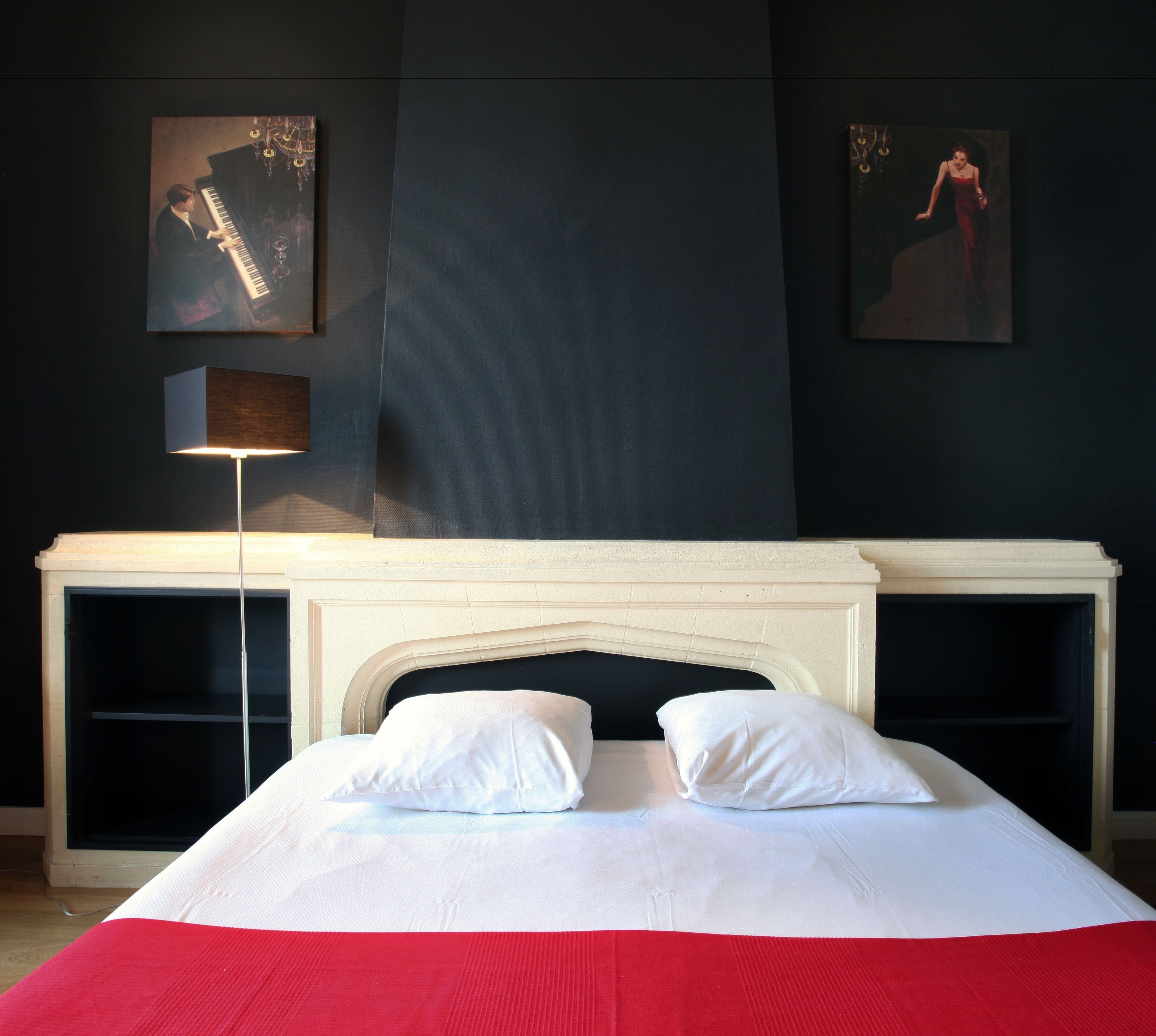 Un dormitorio con cama, mesita de noche, lámpara y dos cuadros en la pared.