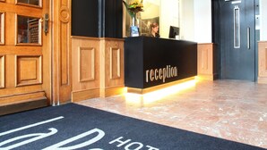 A hotel reception area with a wooden reception desk, a black reception counter, and a reception sign. - Hotel La Royale (Leuven)