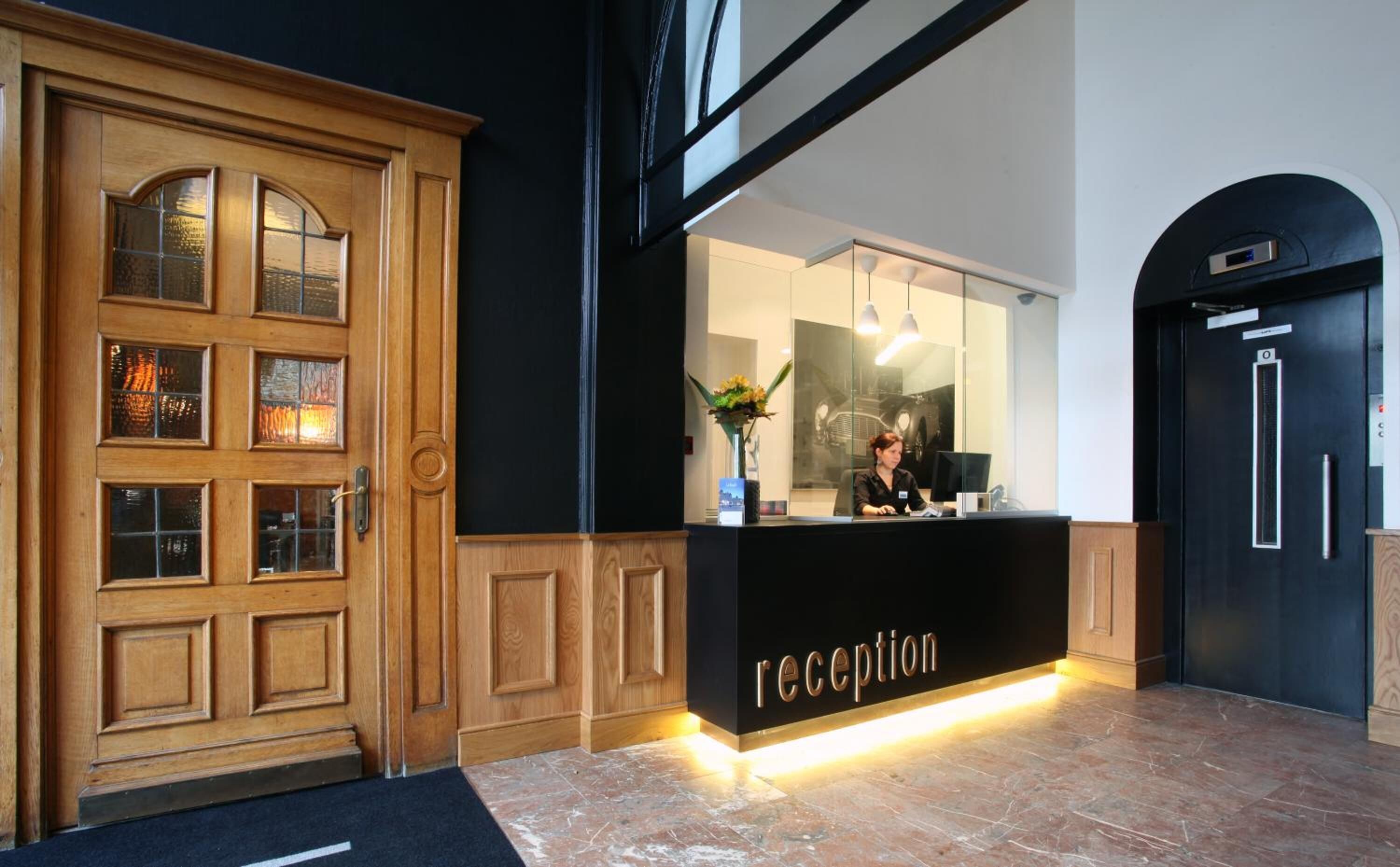 A reception area with a wooden door, a black reception desk, and a receptionist.