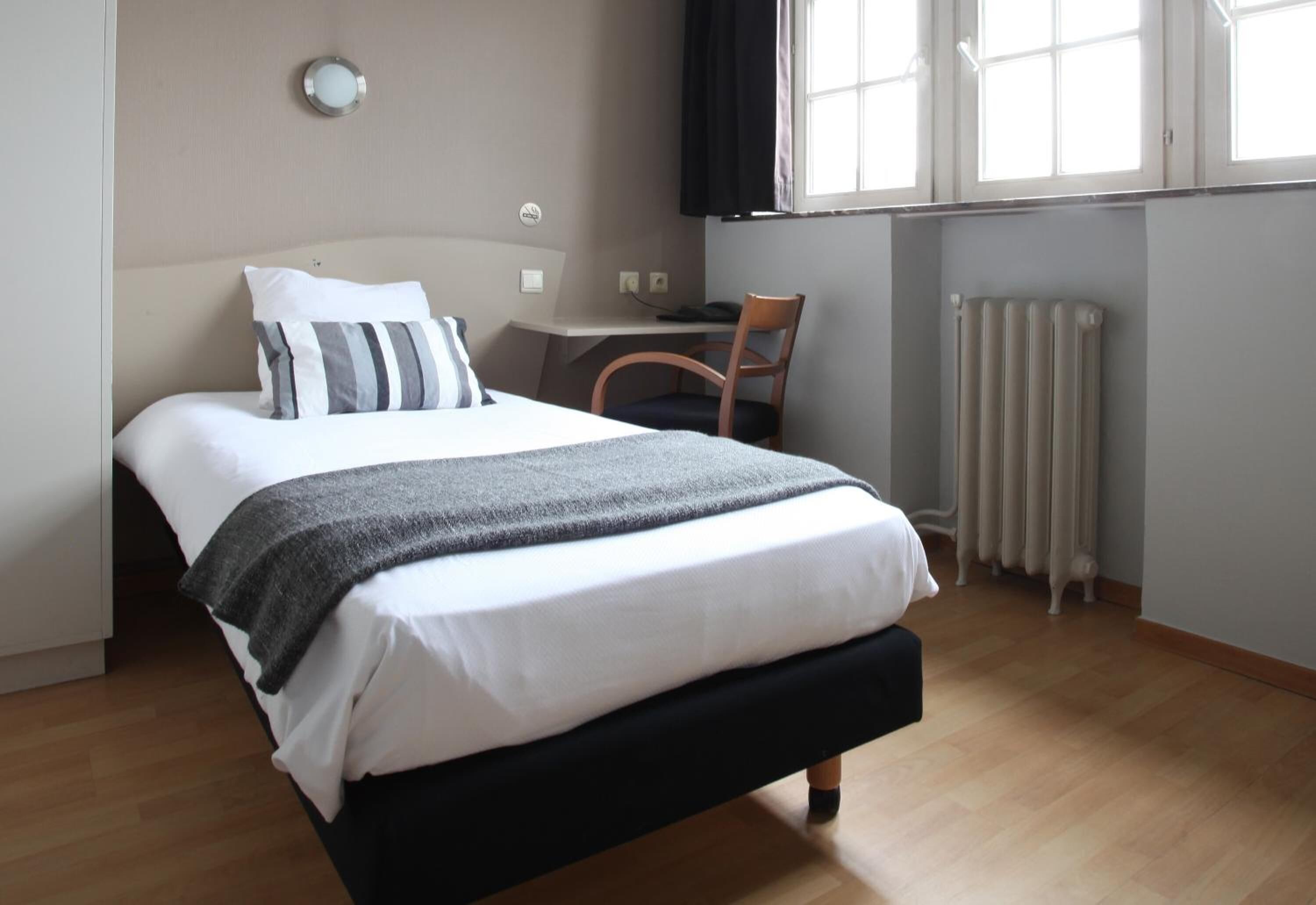Un dormitorio con cama, escritorio, silla y radiador.
