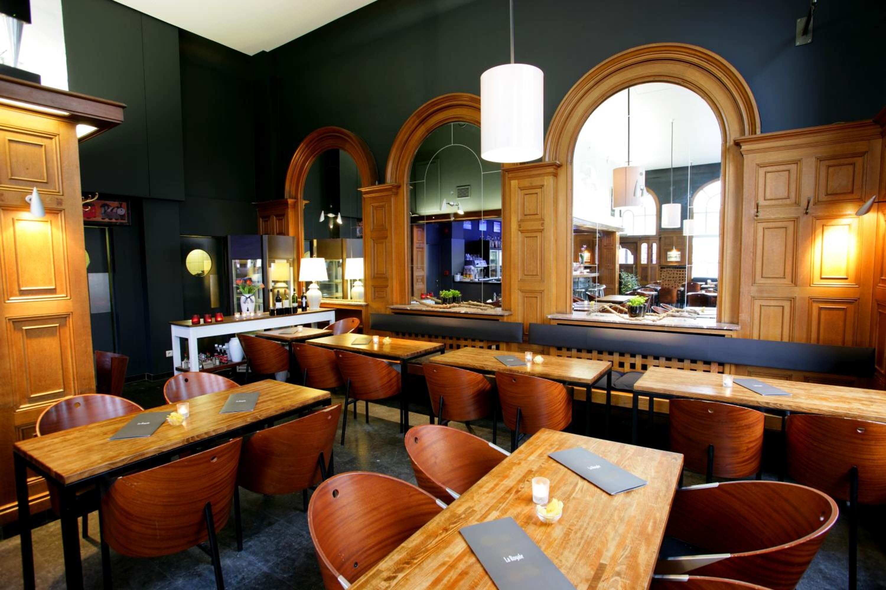 Un restaurante con mesas y sillas de madera, una zona de bar y amplios ventanales en arco.