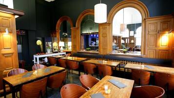 Un restaurante con mesas y sillas de madera, una zona de bar y amplios ventanales en arco.