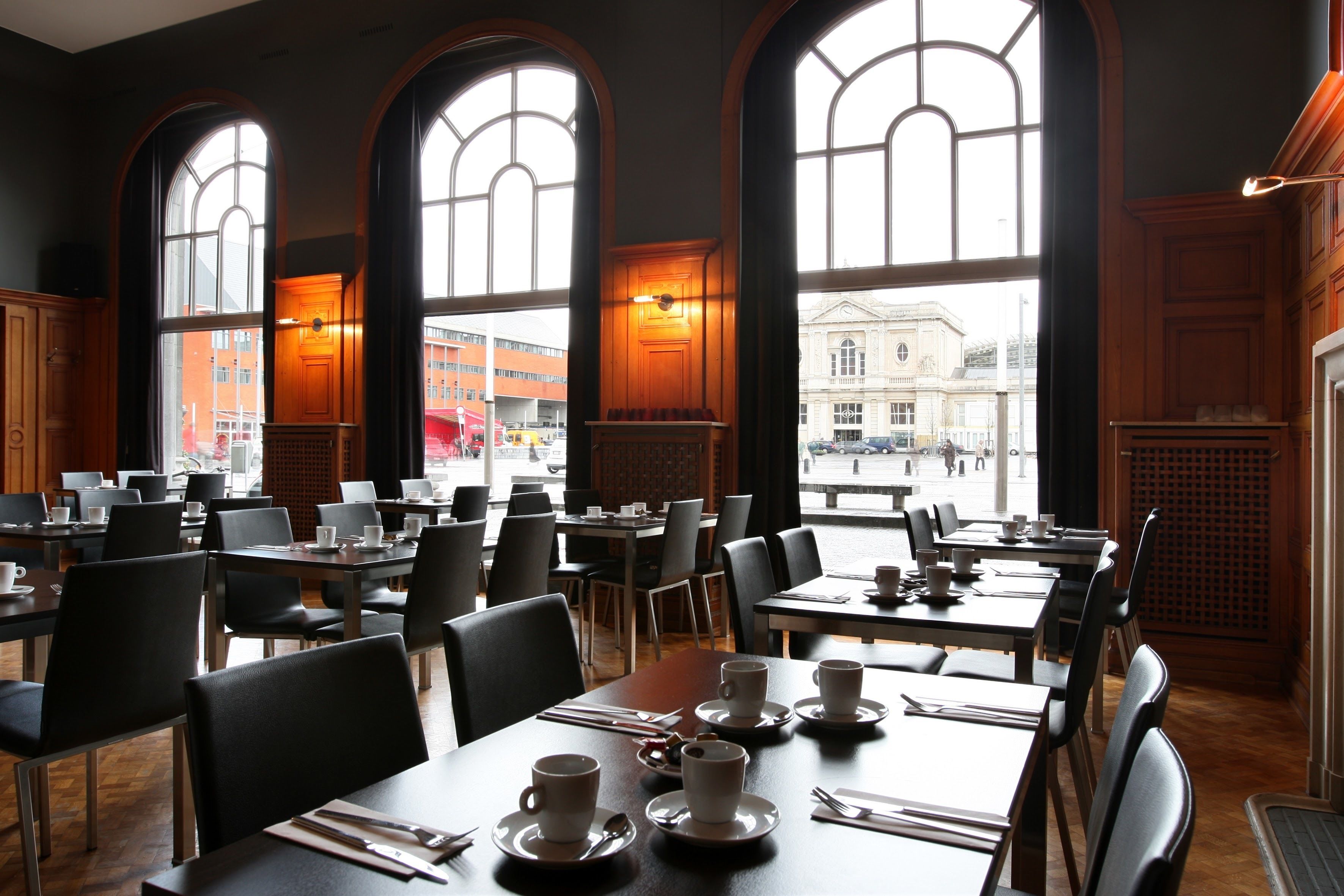 Un café spacieux, doté de nombreuses tables et chaises, de grandes fenêtres en arc de cercle et offrant une vue sur la rue.