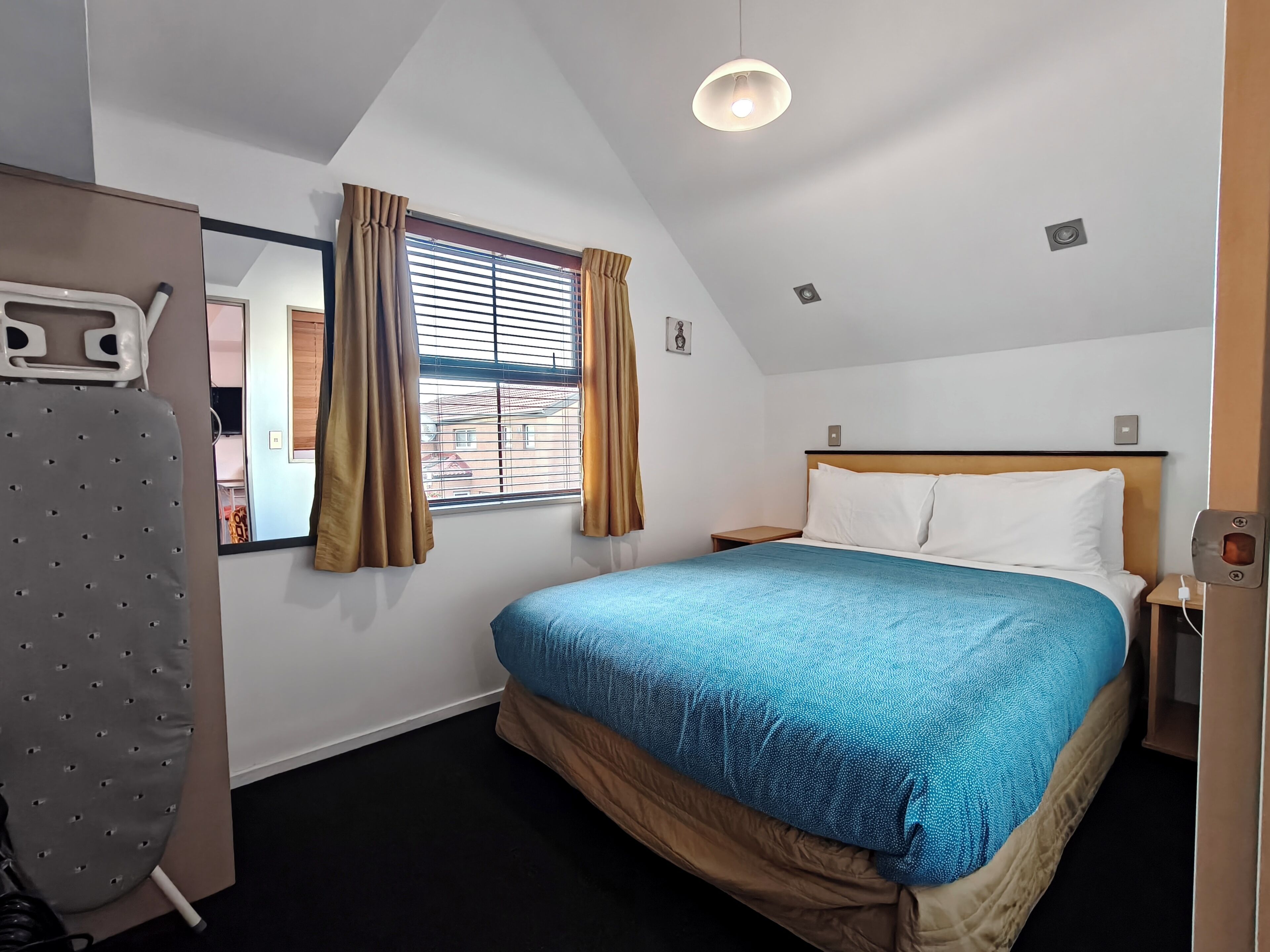 A hotel room with a bed, a nightstand, a lamp, a window with curtains, and a ceiling light.