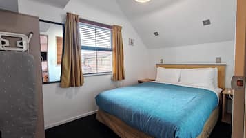 A hotel room with a bed, a nightstand, a lamp, a window with curtains, and a ceiling light.