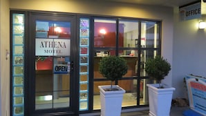 La entrada del motel Athena, con una recepción, un letrero que indica que está abierto y dos plantas en macetas.