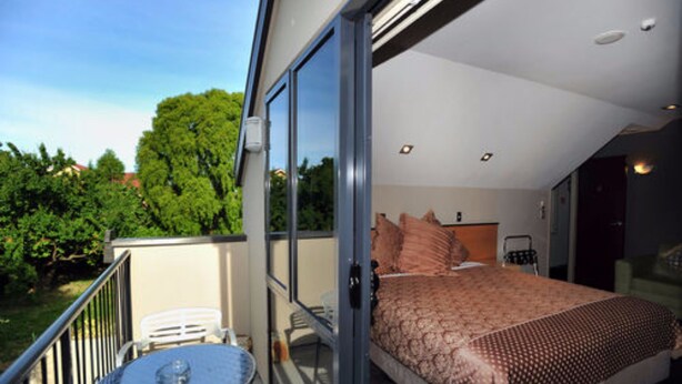 Un dormitorio con una cama grande, un balcón con mesa y sillas, y vistas a zonas verdes.