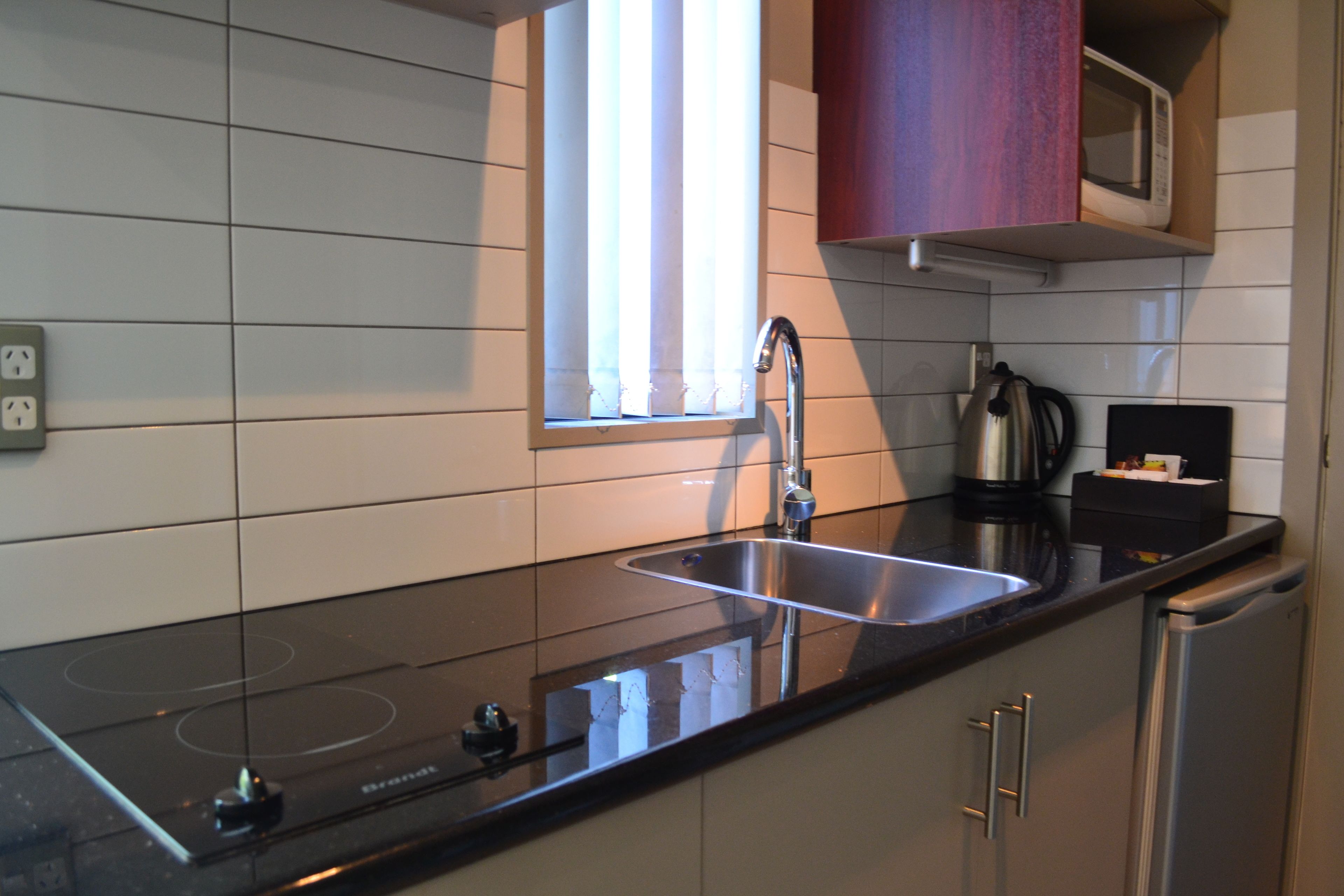 A modern kitchen with a black countertop, stainless steel sink, and a built-in induction cooktop.