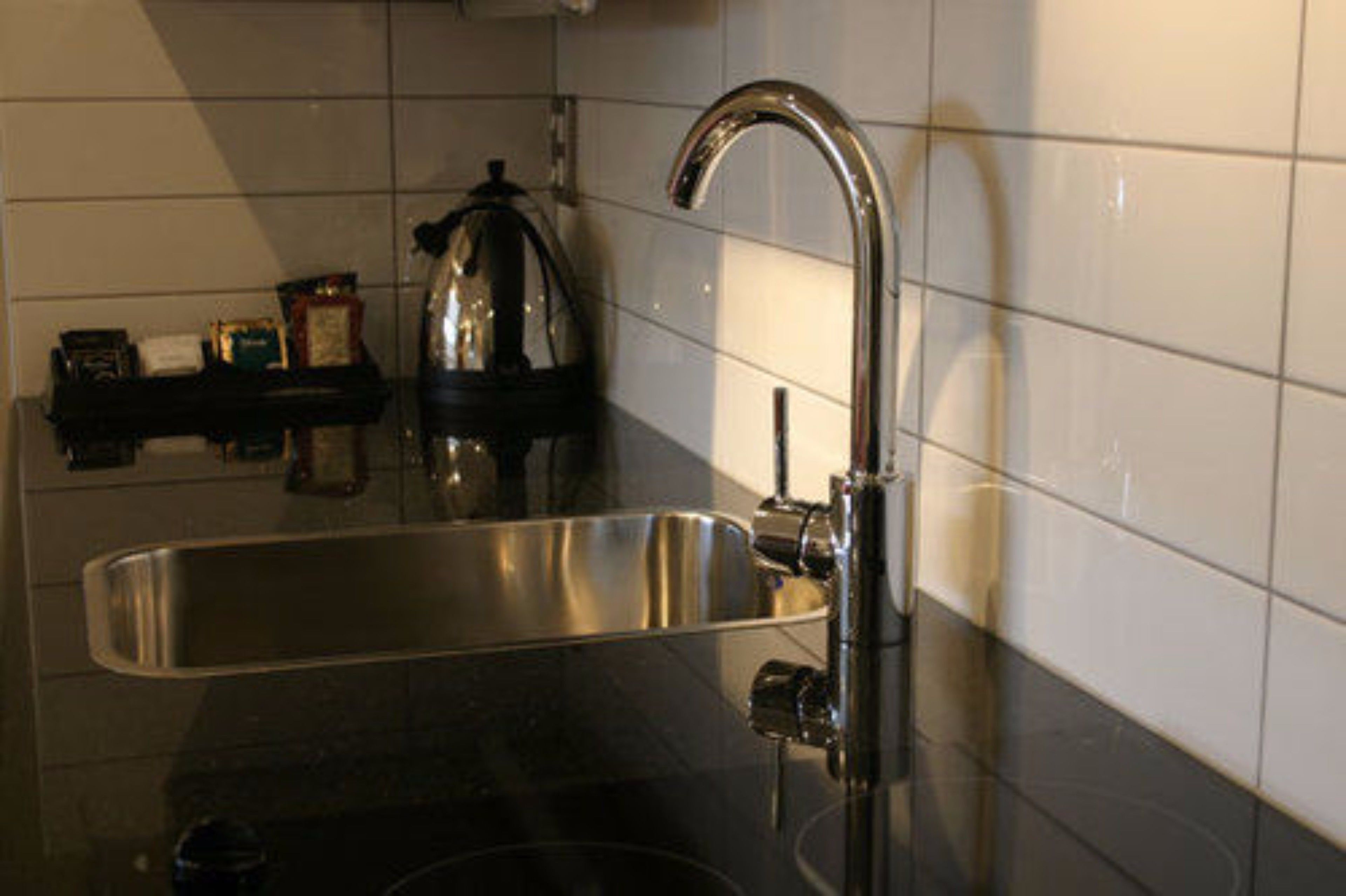 Una cocina con un lavamanos de acero inoxidable, una encimera negra y una tetera en un estante.