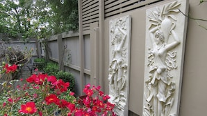 Un jardín con flores rojas y dos esculturas en relieve blancas sobre una pared.