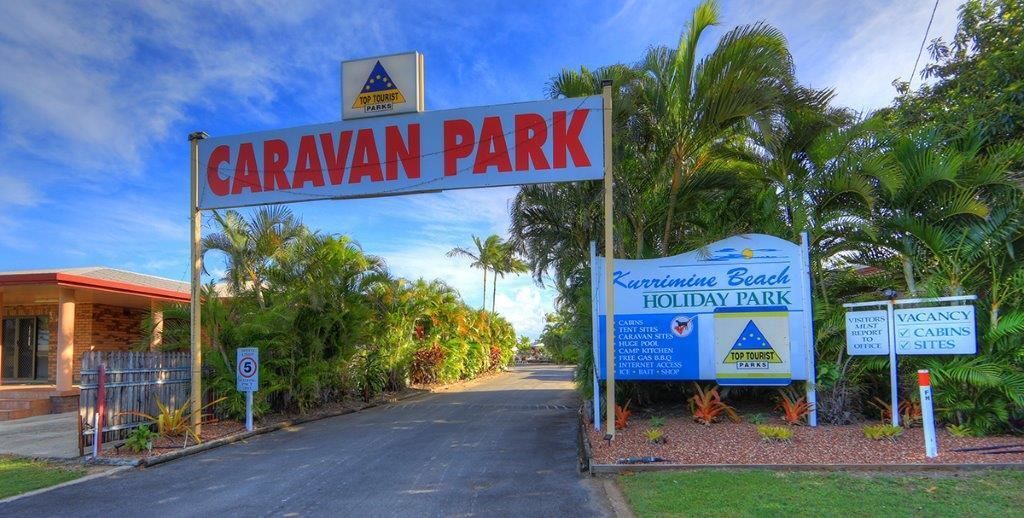 A sign for Caravan Park with a clear road leading to it, surrounded by lush greenery and palm trees.