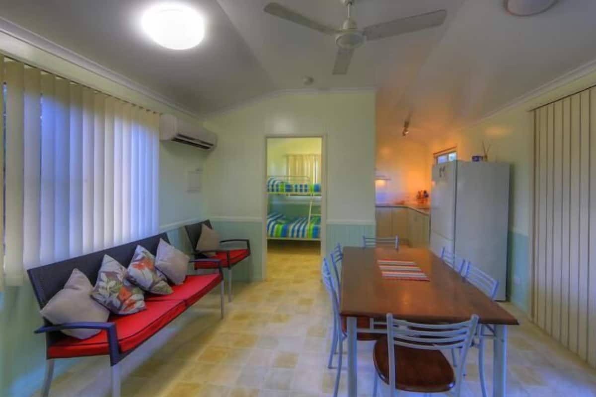 Un espacio habitable compacto con comedor, un sofá con cojines, un ventilador de techo y un refrigerador.