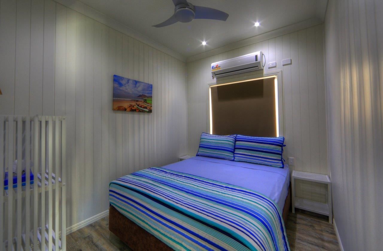 A bedroom with a bed, a ceiling fan, an air conditioning unit, and a painting on the wall.