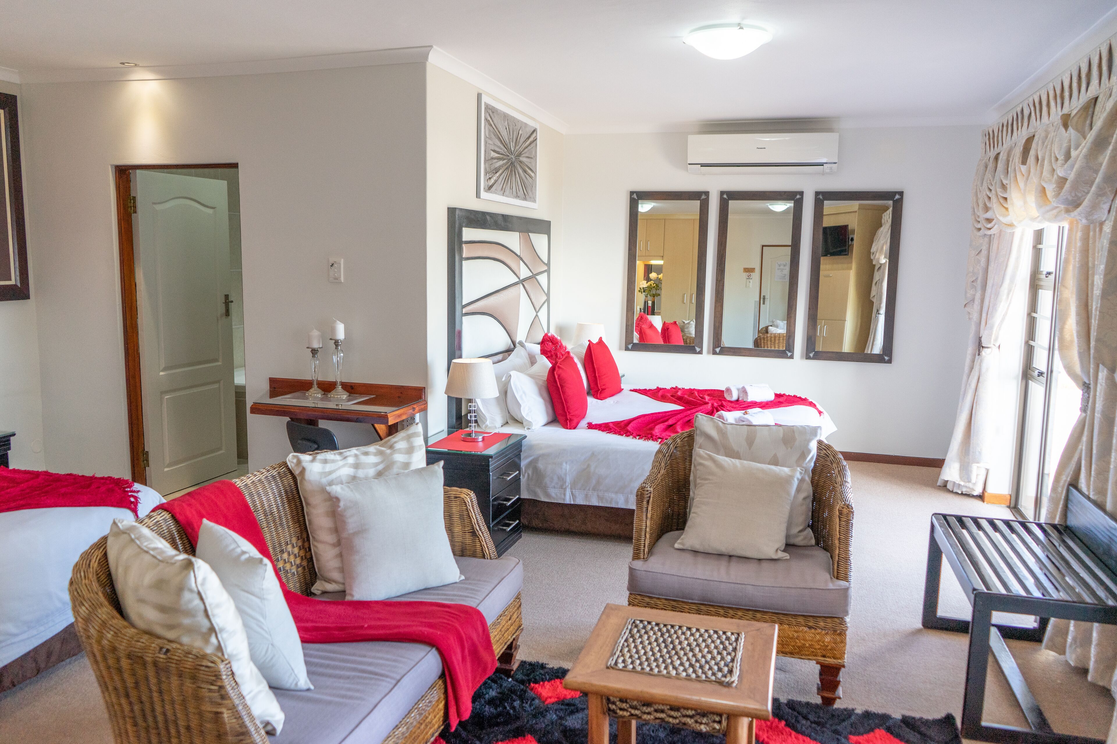 A well-lit, modern hotel room with a large bed, two sofas, a small table, and a mirror.