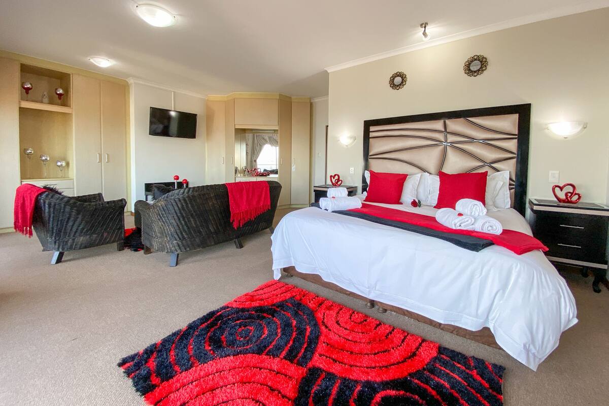 A hotel room with a large bed, two armchairs, a TV, and a wardrobe.