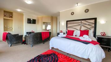A hotel room with a large bed, two armchairs, a TV, and a wardrobe.