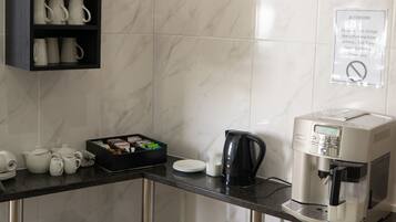 Et kompakt køkken med kaffemaskine, tepakke og skraldespand.