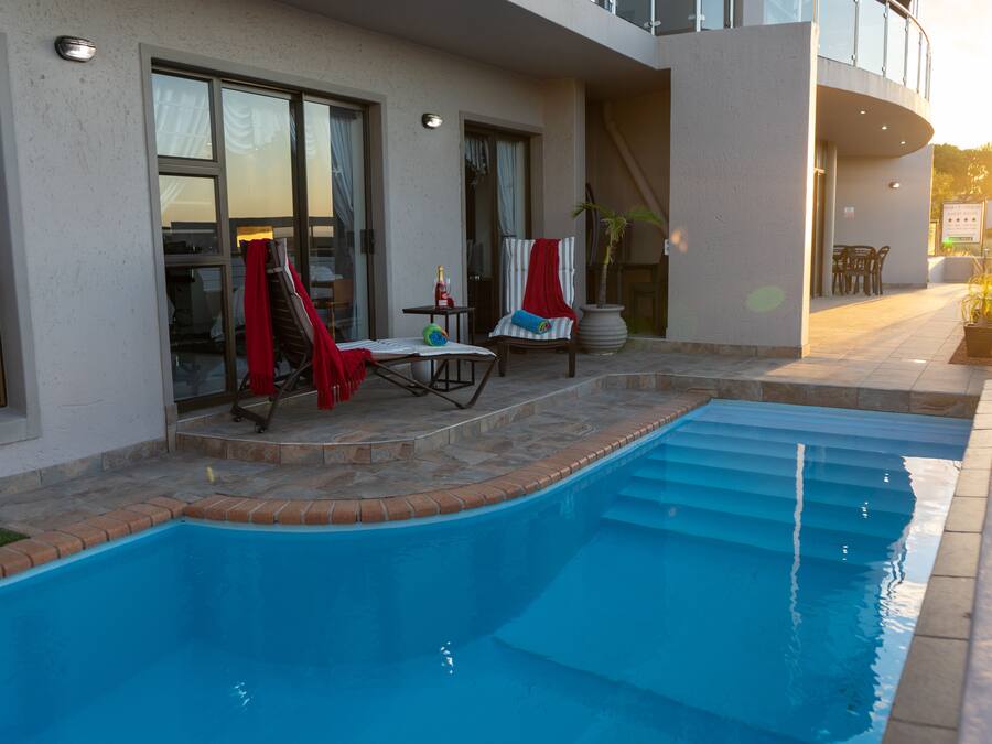 Una piscina con un patio soleggiato, una zona salotto coperta e una scala che conduce a un piano superiore.