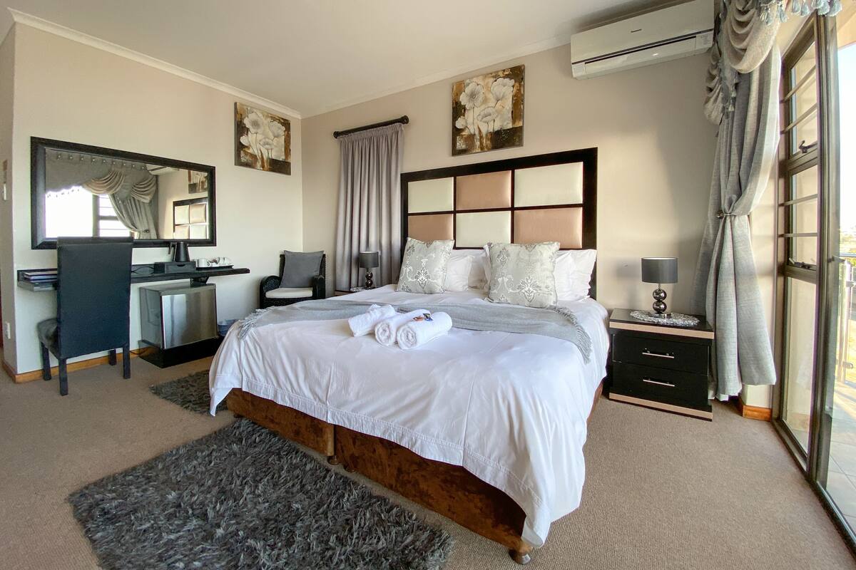 A hotel bedroom with a large bed, a desk, a chair, a dresser, and a window with curtains.