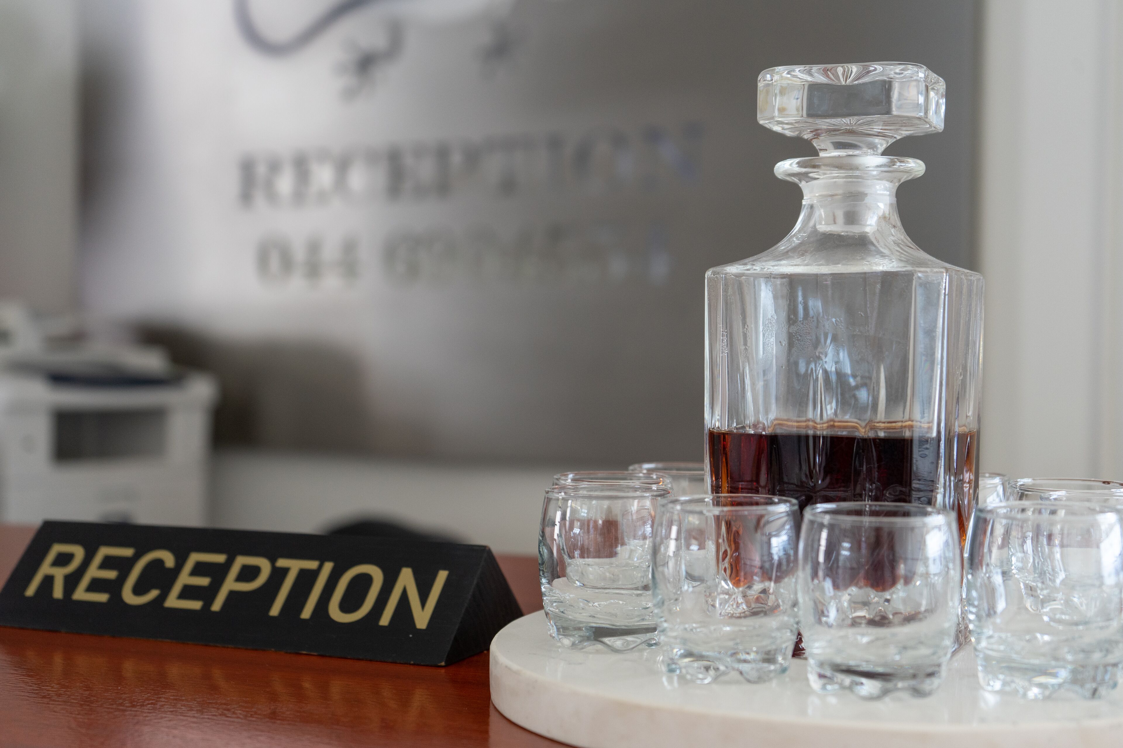 A reception area with a sign labeled "RECEPTION" and a decanter filled with a dark liquid, surrounded by empty glasses on a marble table.