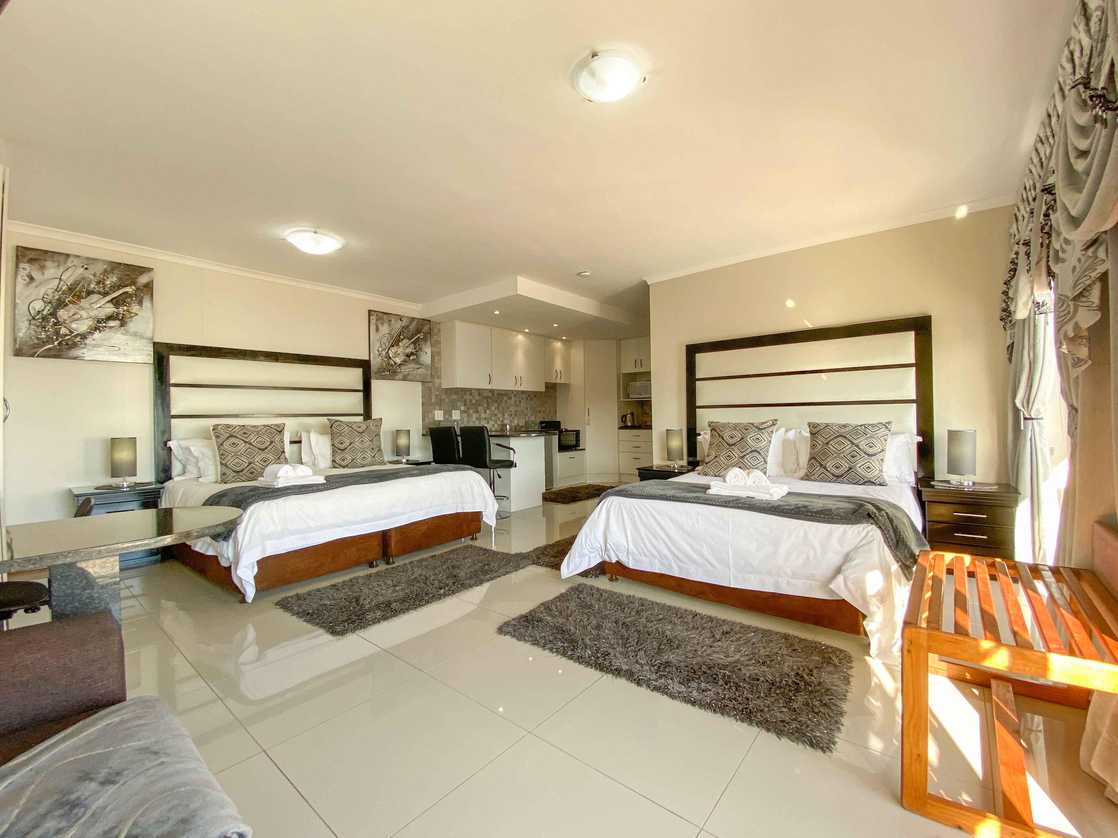 Habitación de hotel moderna con dos camas, una kitchenette pequeña y un baño.