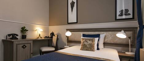 Une chambre d’hôtel comprenant un lit, des tables de chevet, un bureau avec une lampe, un téléphone et une plante.