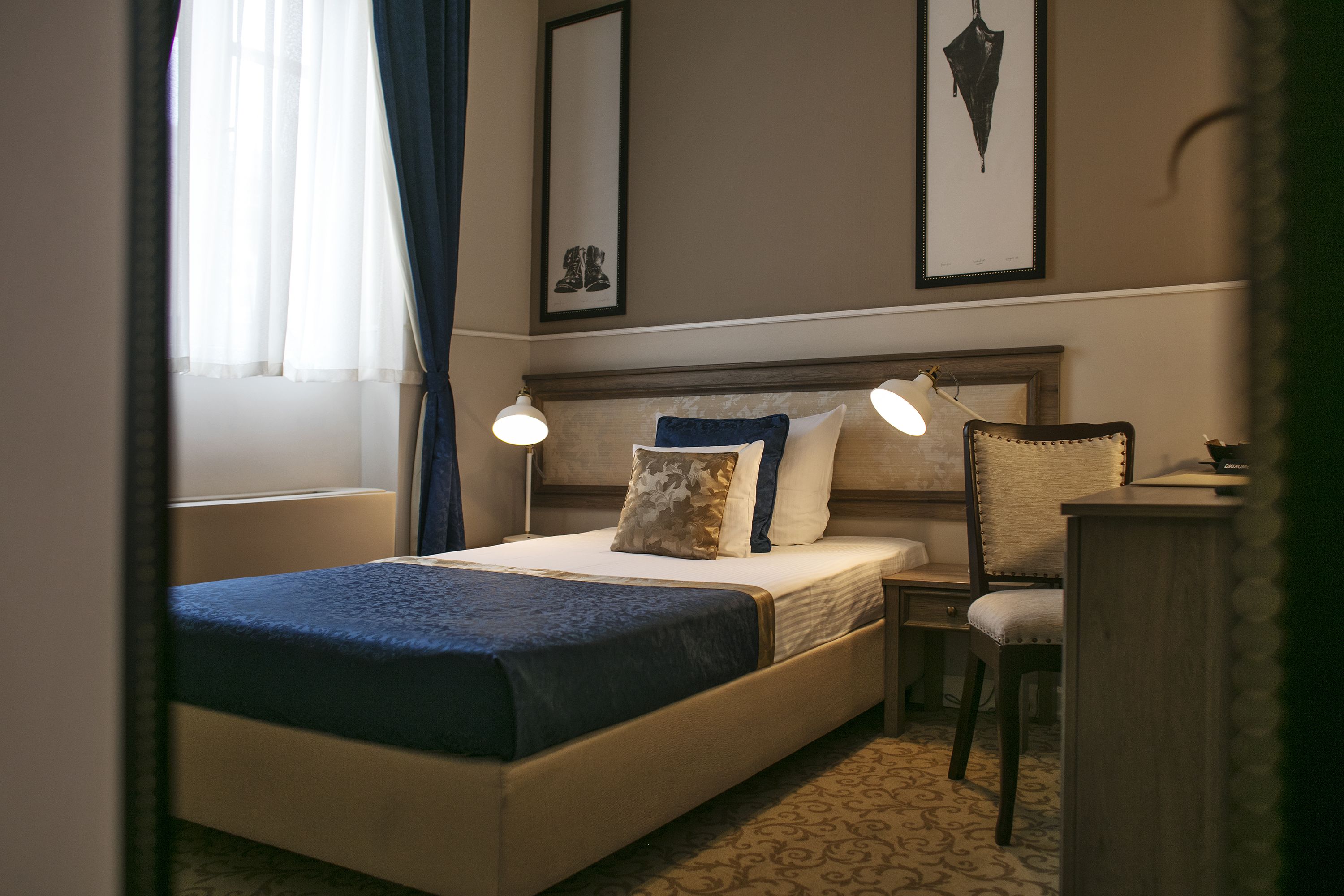 Ett hotellrum med en säng, sänglampor, en stol, ett skrivbord och inramade konstverk på väggen.