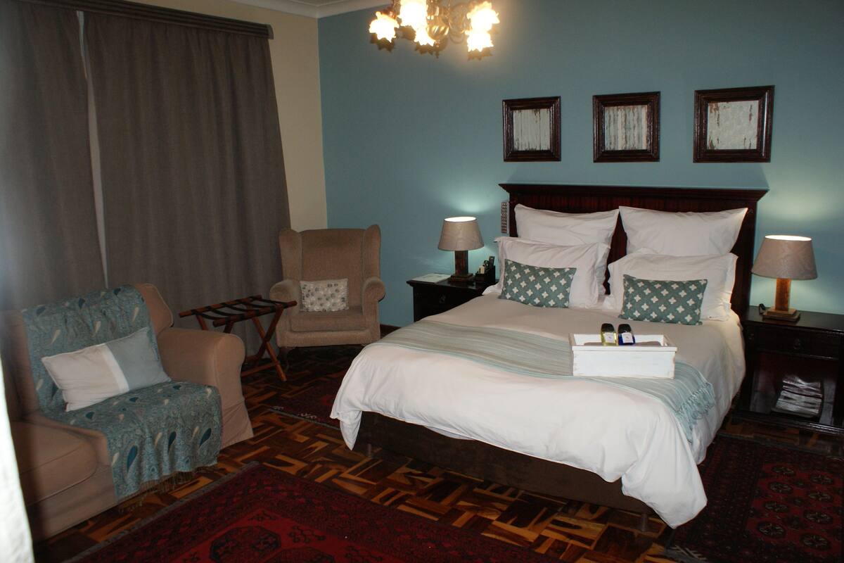 Quarto de hotel com uma cama grande, duas mesas de cabeceira, uma cadeira e um lustre.