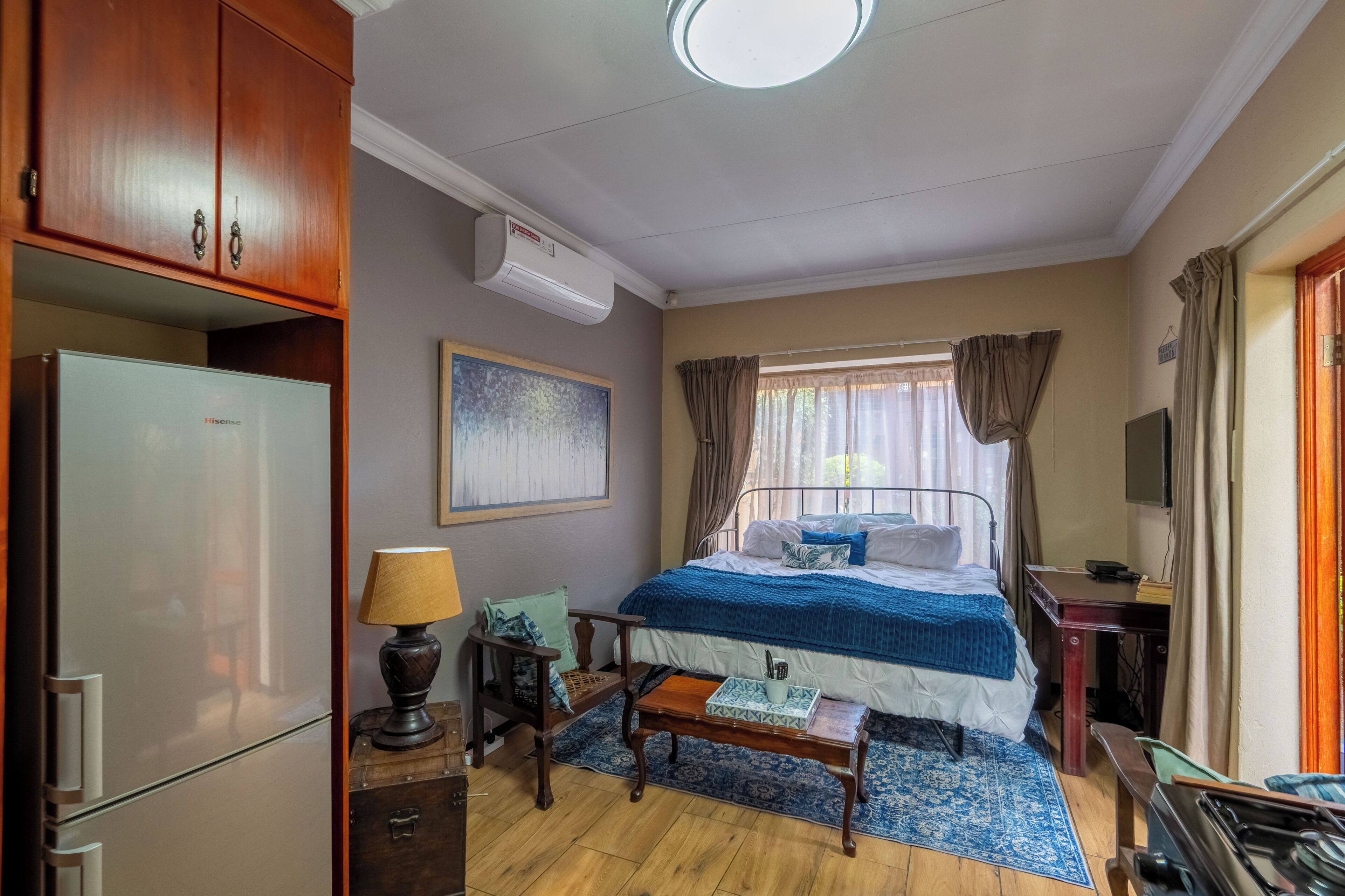 Un dormitorio con cama, escritorio, lámpara, refrigerador y aire acondicionado.