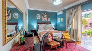 Un dormitorio con una cama grande, una silla, un escritorio, un espejo y una ventana con cortinas.