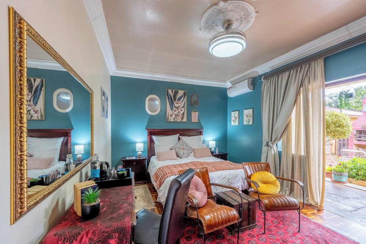 Quarto com uma cama grande, uma cadeira, uma escrivaninha, um espelho e uma janela com cortinas.