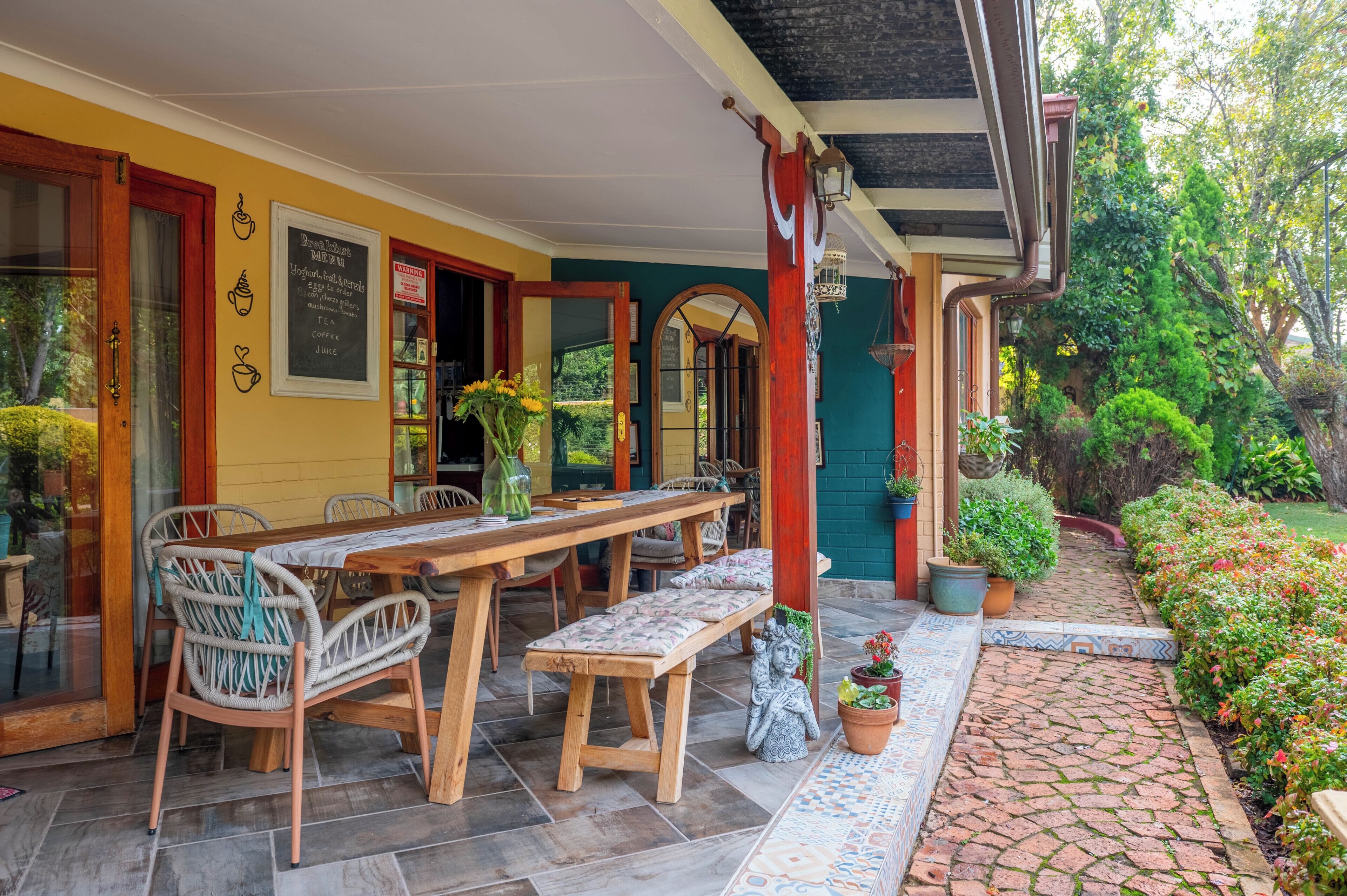 Un patio cubierto con una mesa y sillas de madera, un banco y plantas en macetas.