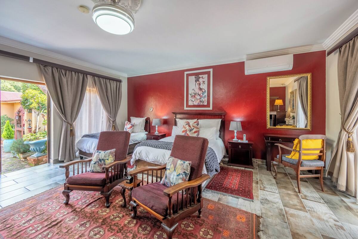 Quarto com cama, duas cadeiras, escrivaninha, espelho e janela com cortinas.