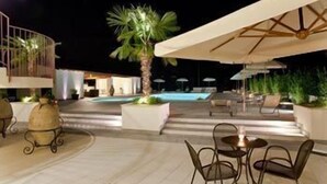 Een terras buiten met een zwembad, lounge stoelen en een eettafel.