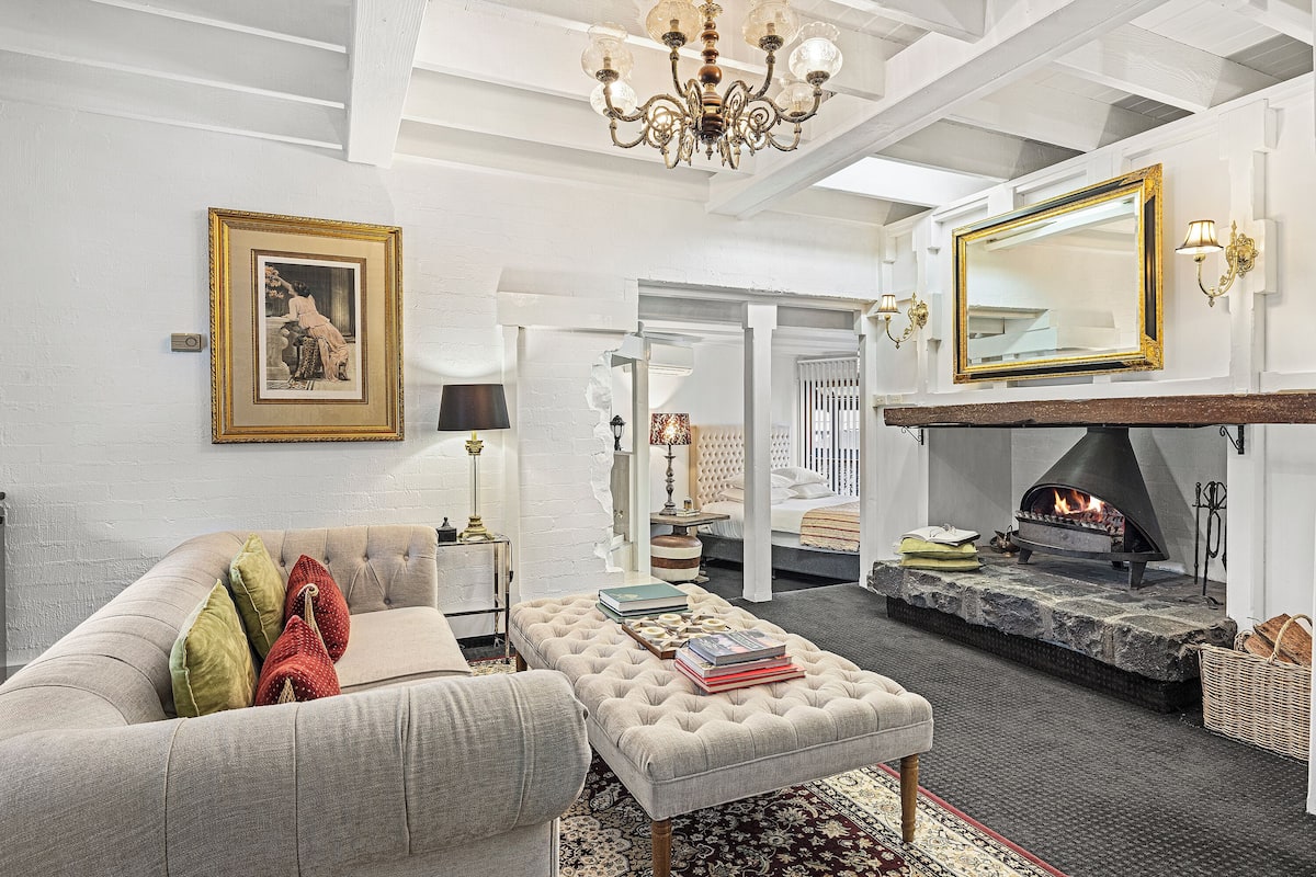 A living room with a fireplace, a sofa, an ottoman, and a large mirror.