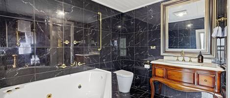 A bathroom with a large bathtub, a vanity with a mirror, and black marble tiles.