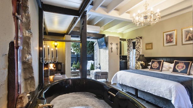 A bedroom with a large bathtub, a bed with a white bedspread, and a chandelier. - The Loft In The Mill Boutique Accommodation (Olinda)