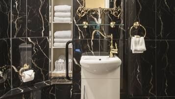 Une salle de bain avec des toilettes blanches, un lavabo blanc et une baignoire. On y trouve un miroir avec un cadre orné et un porte-serviettes avec une serviette.