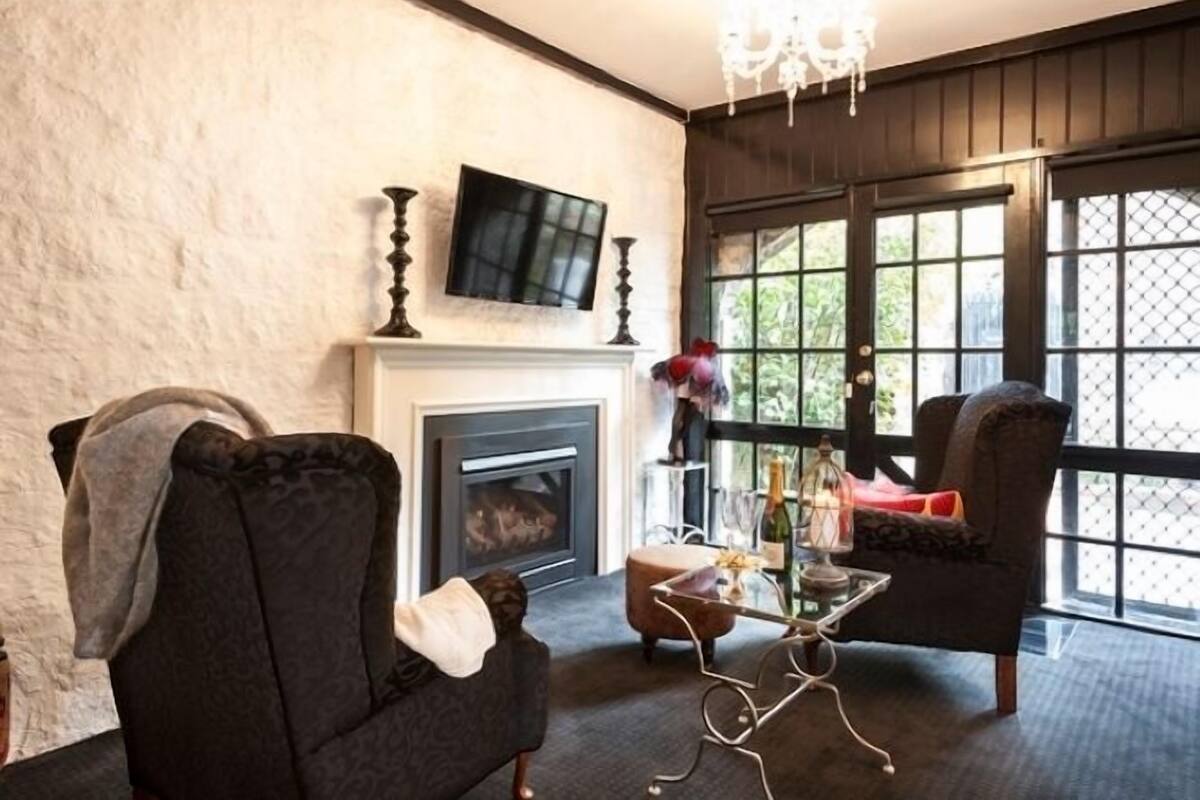 A living room with a fireplace, a television, and a view through large windows.