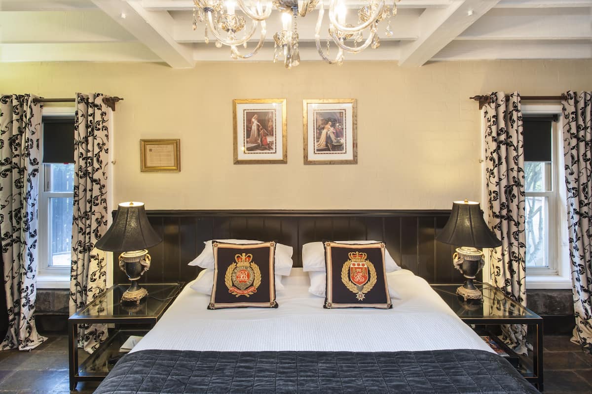 A hotel room with a large bed, two framed pictures on the wall, a chandelier, and curtains with a floral pattern.
