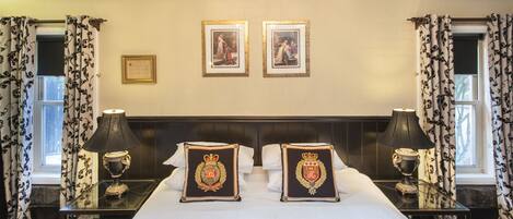 A hotel room with a large bed, two framed pictures on the wall, a chandelier, and curtains with a floral pattern.