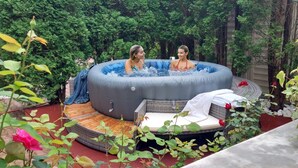 Ett bubbelbad i en trädgård med en bänk av rotting och ett litet bord.
