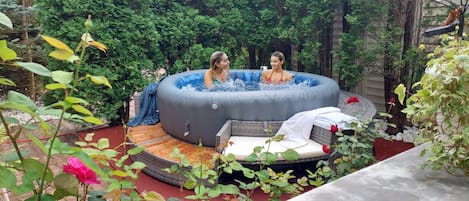 A hot tub in a garden with a wicker bench and a small table.