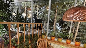 En mysig, inbyggd balkong med träräcken, krukväxter, möbler i rotting och en stor, vävd lampa.
