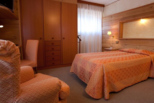 A bedroom with a bed, a chair, a wardrobe, and a nightstand. - Hotel Pavillon (Courmayeur)